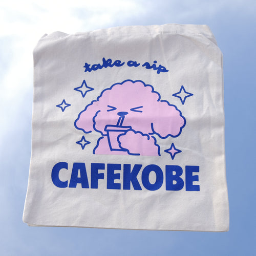 White tote bag with pink poodle graphic and 'CAFEKOBE' text on a textured surface.
